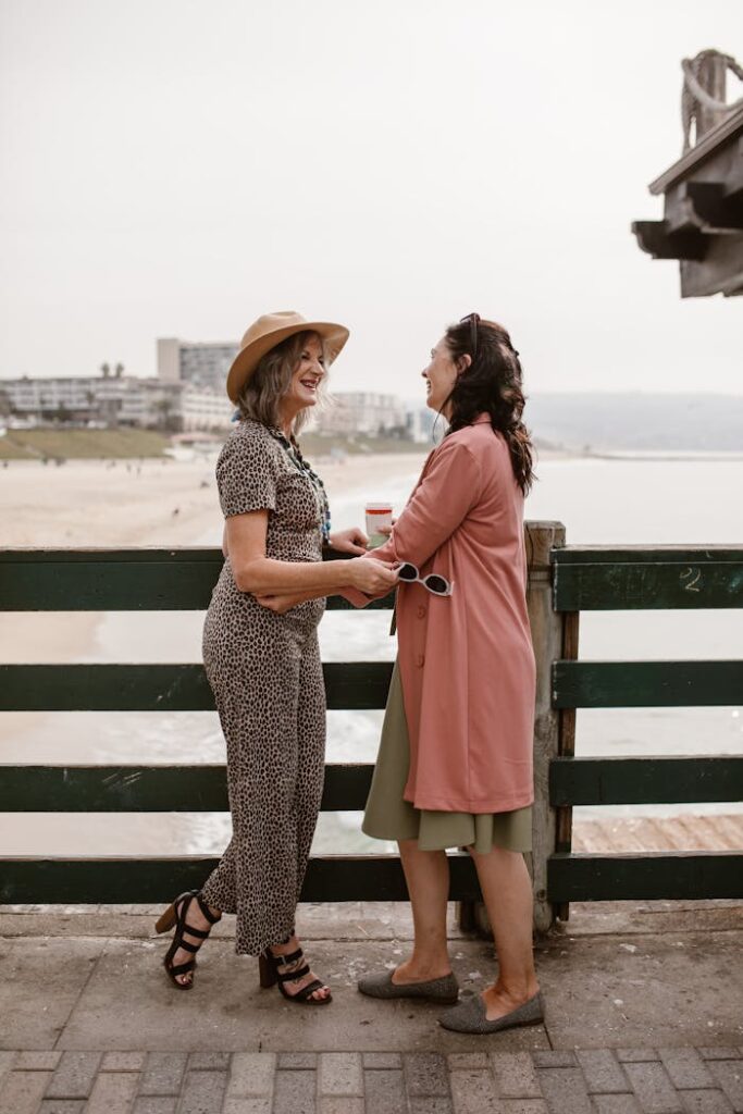 pexels photo 6539972 Two women sharing laughter and holding hands by the beach, embracing friendship and joy.